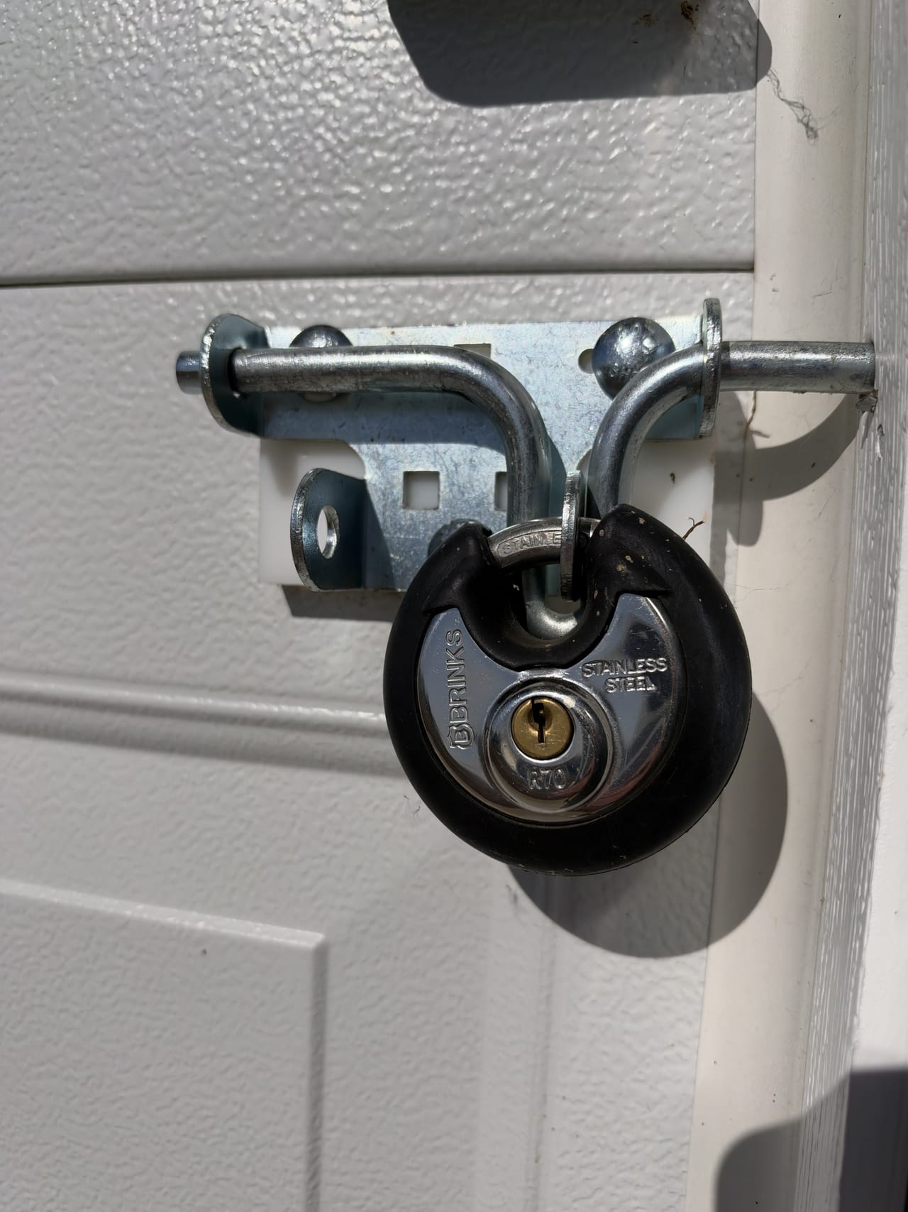 A disc padlock through the latch of a white overhead door